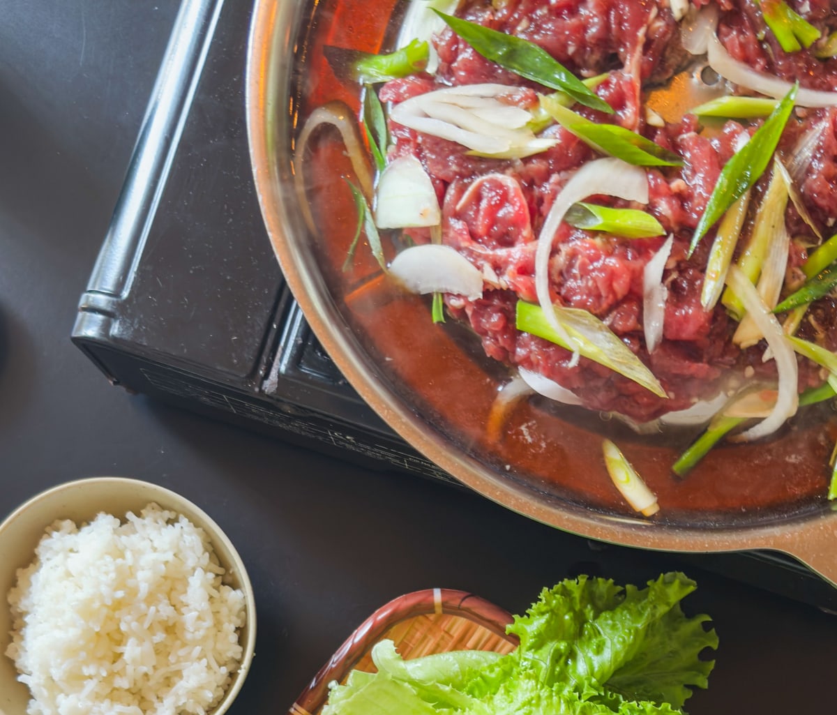 Marinated bulgogi beef with onion and scallions in a tabletop pan, served with rice, lettuce and side dishes