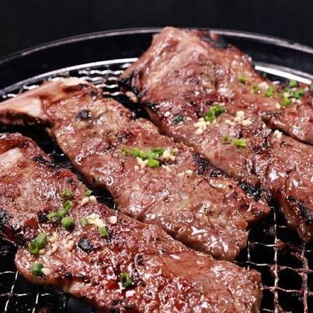 Marinated galbi short ribs grilling over charcoal, topped with scallions and sesame