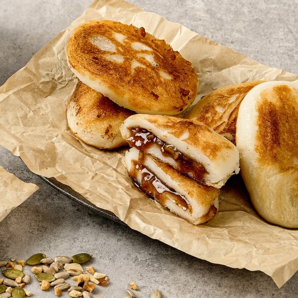 Hotteok pressed flat and golden, one cut open to show the melted brown sugar and nut filling
